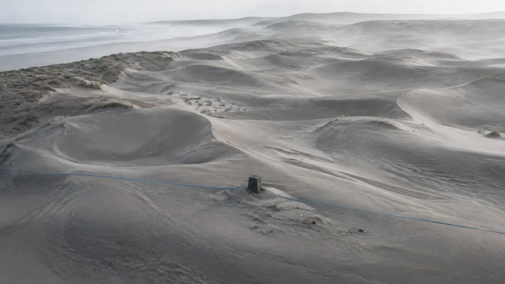 Wind-shaped dunes crossed by a blue survey line and fixed marker, representing changing AI answers measured against a stable baseline